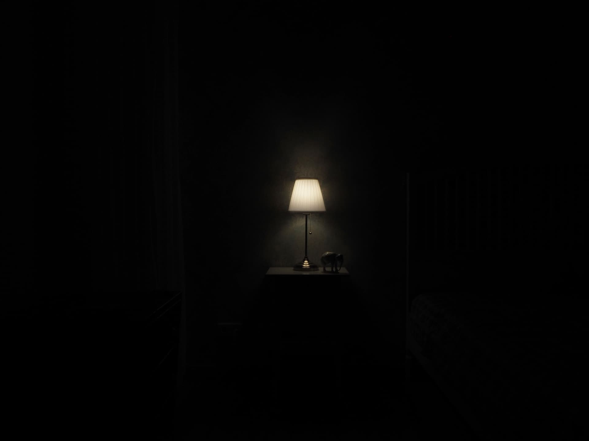 A single lamp lit on a nightstand in an otherwise dark, bare room